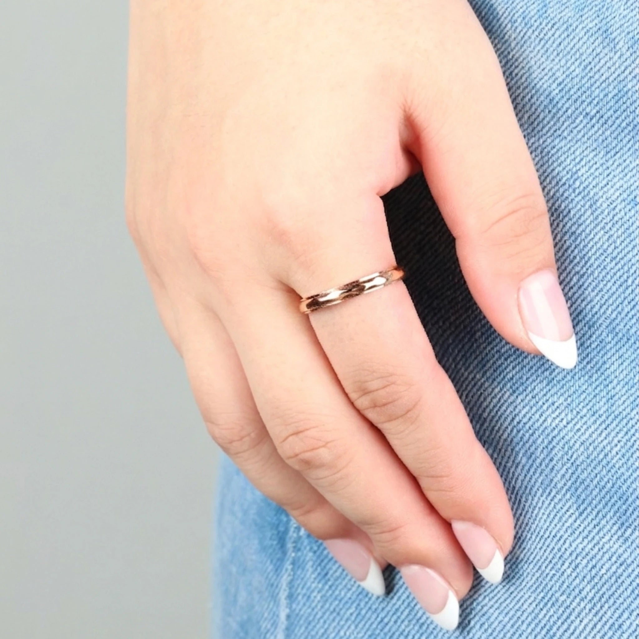 Hand van een vrouw met verzorgde nagels tegen een achtergrond van blauwe jeans, dragend een minimalistische roségouden Amara anti-stress ring.