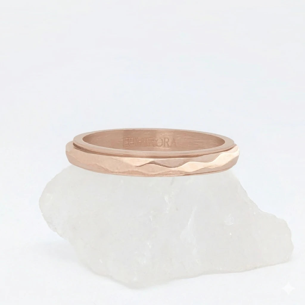 Roségouden Amara fidget ring van waterproof roestvrij staal, ontworpen met een elegante gefacetteerde afwerking, gepresenteerd op een witte steen.