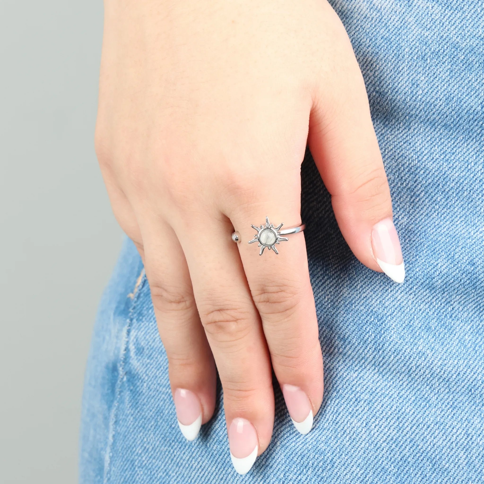 Zilveren Solar anxiety ring met zonvorm en heldere steen, gedragen op jeans – elegante verstelbare ring die helpt spanning los te laten