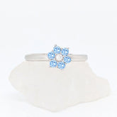 Zilveren Aqua fidget ring met een lichtblauwe bloem van kristallen liggend op een witte ruwe steen