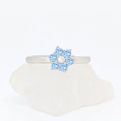 Zilveren Aqua fidget ring met een lichtblauwe bloem van kristallen liggend op een witte ruwe steen