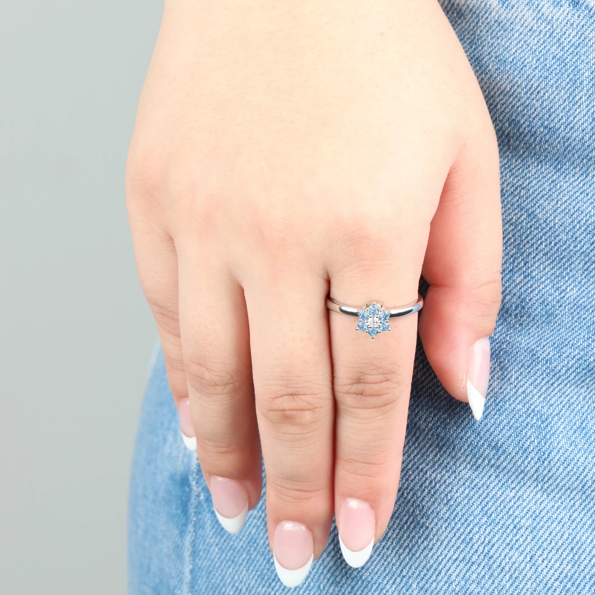 Close-up van de zilveren Aqua stress ring met blauwe steentjes gedragen op een spijkerbroek.