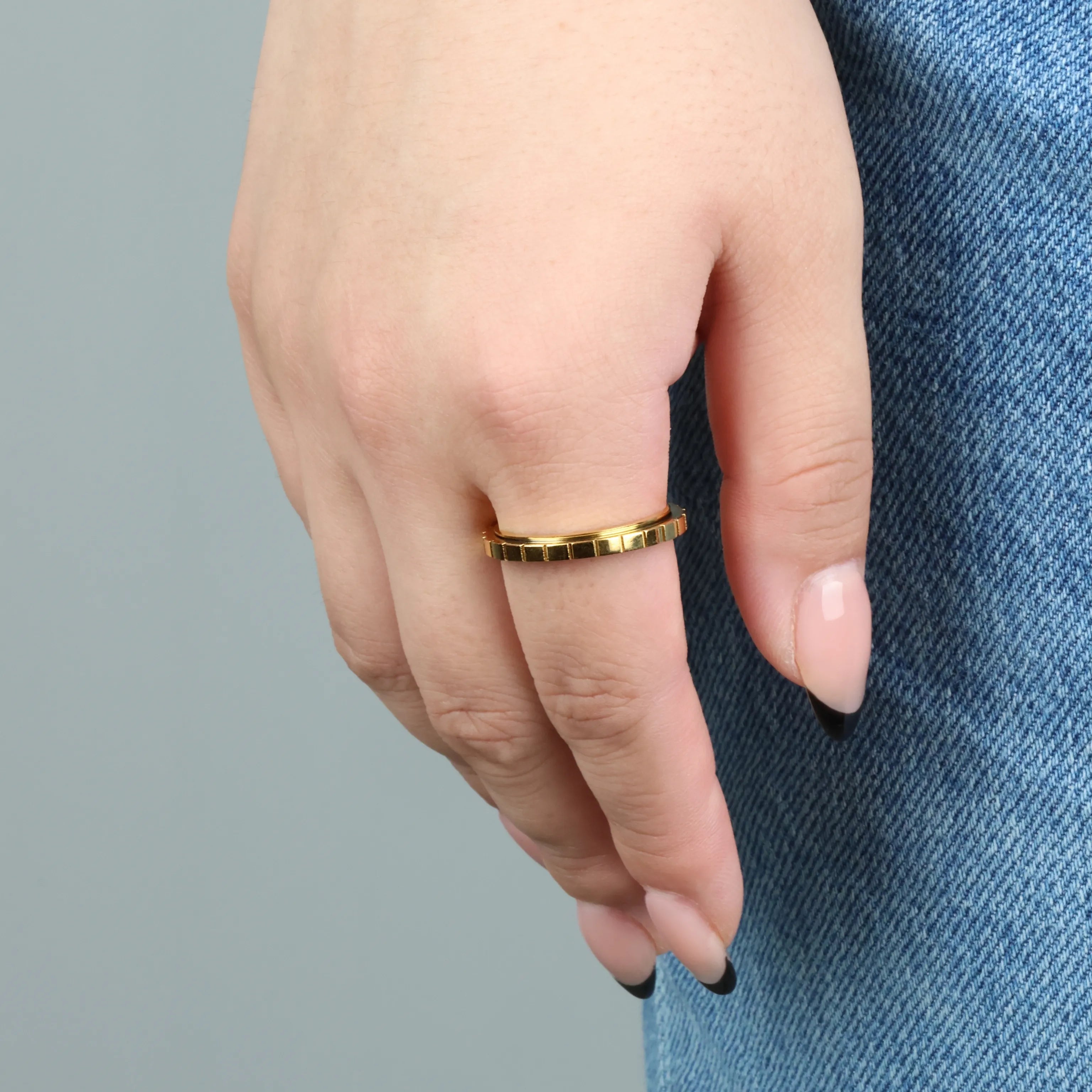 Gouden Axis fidget ring met strak groevenpatroon – handfoto met spijkerbroek achtergrond – Luminora