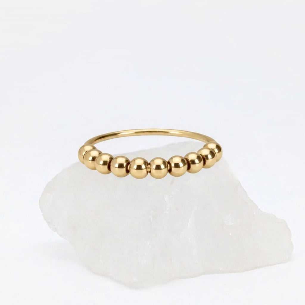 Gouden Classic Bead fidget ring van RVS met los te bewegen kralen, elegant gepresenteerd op een witte steen.