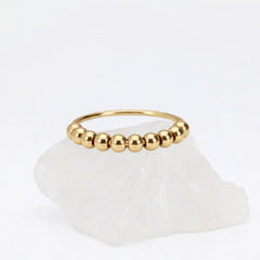 Gouden Classic Bead fidget ring van RVS met los te bewegen kralen, elegant gepresenteerd op een witte steen.