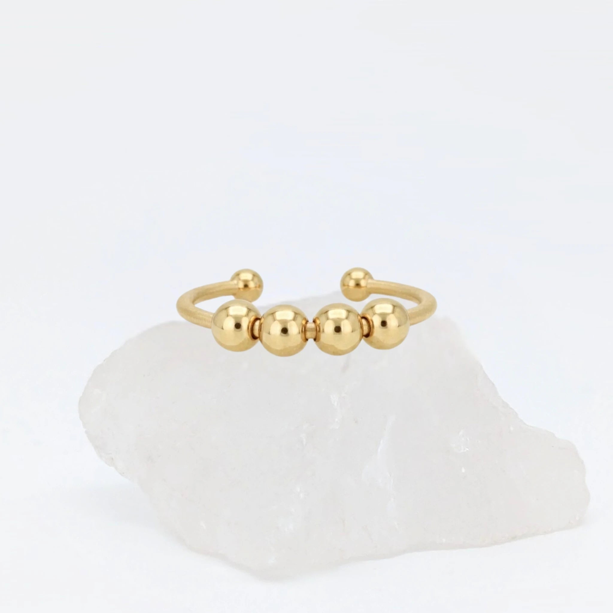 Gouden Core Bead fidget ring met vijf beweegbare balletjes, gepresenteerd op een witte kristallen steen.
