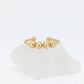 Gouden Core Bead fidget ring met vijf beweegbare balletjes, gepresenteerd op een witte kristallen steen.