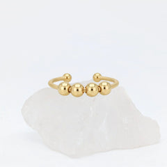 Gouden Core Bead fidget ring met vijf beweegbare balletjes, gepresenteerd op een witte kristallen steen.