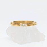Gouden Elara fidget ring met drie subtiele kristallen en textuur, gepresenteerd op een witte steen.
