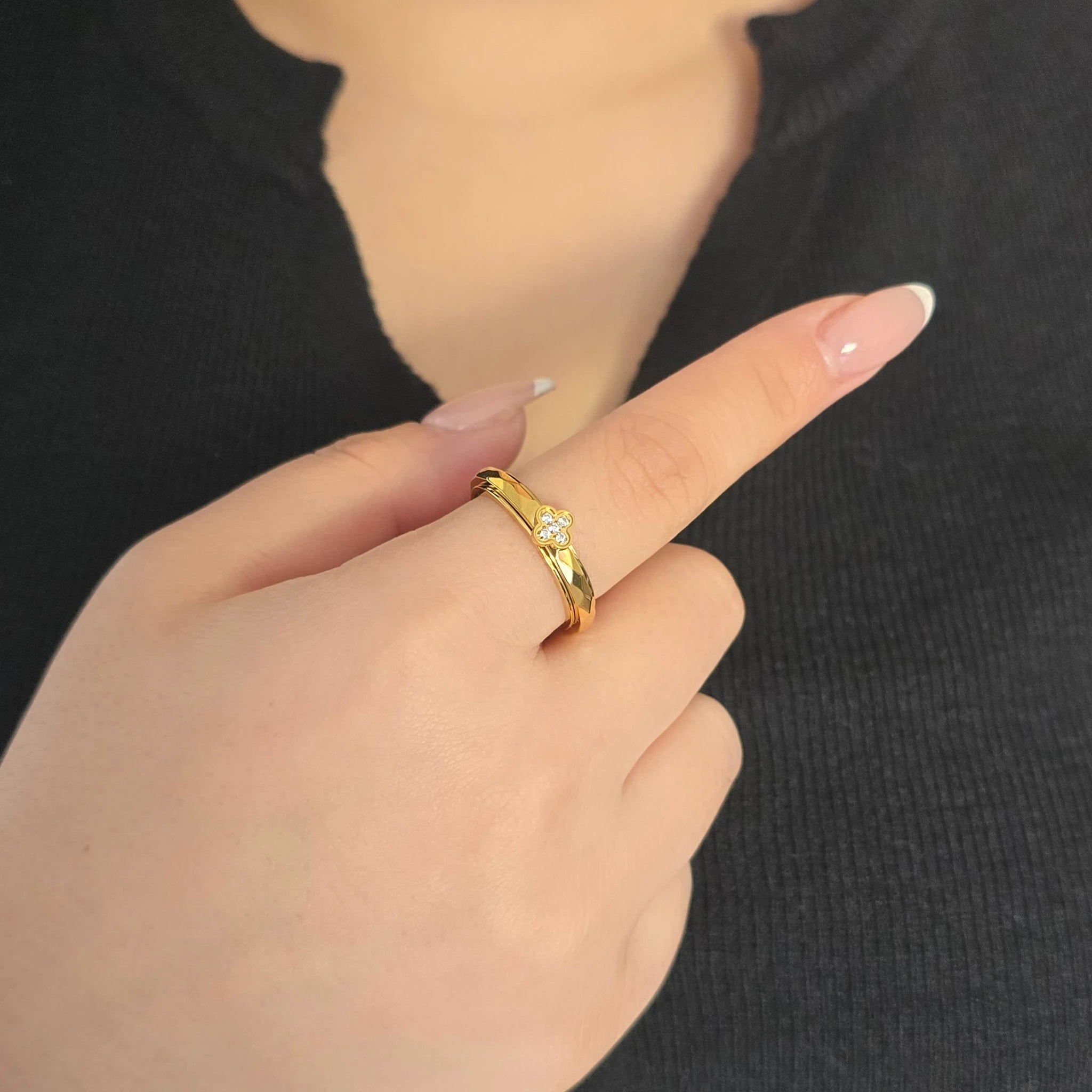 Elegante gouden Clover fidget ring met een met kristallen bezet klavertje vier, gedragen aan de wijsvinger door een model in een zwart topje.