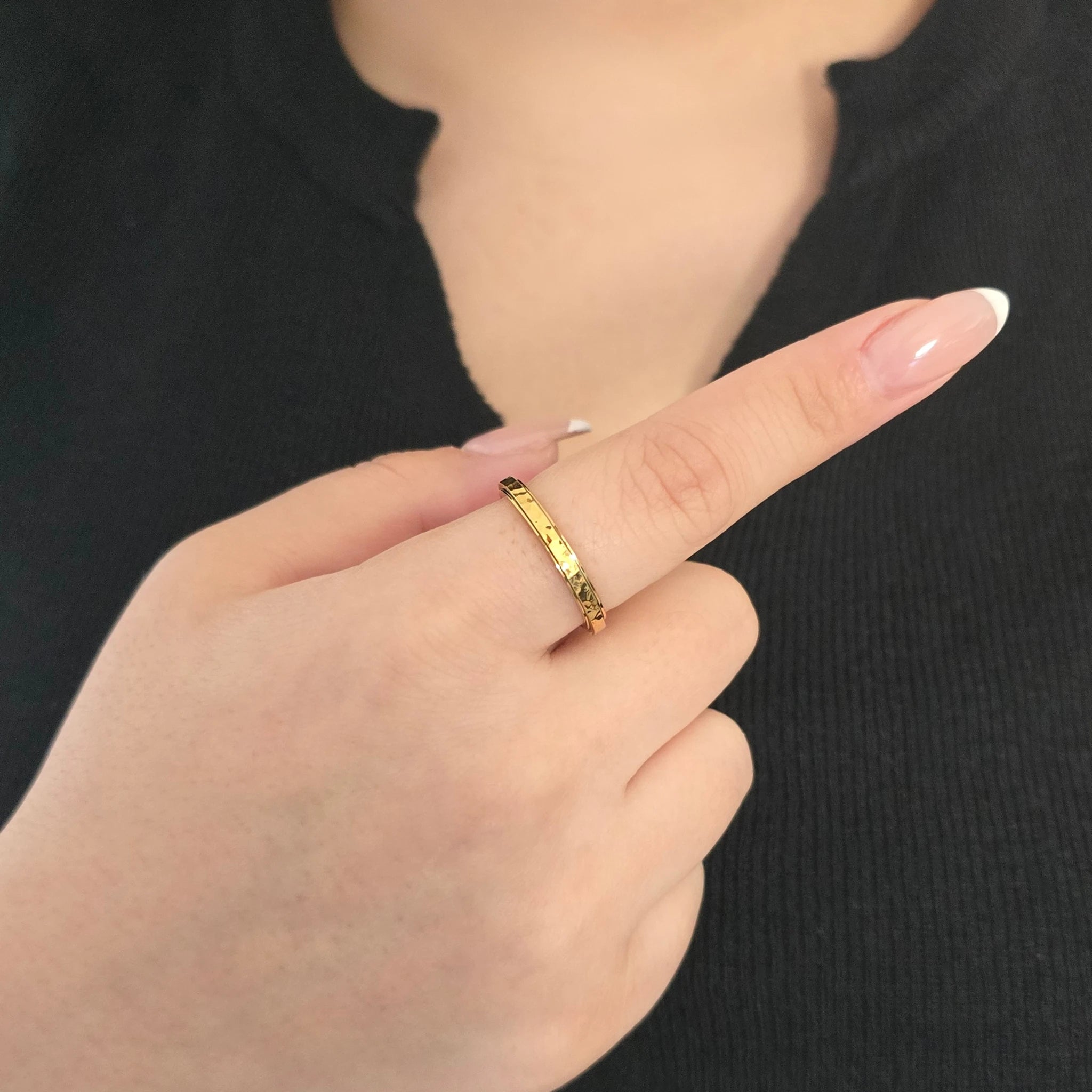 Detailopname van een gouden fidget ring met een bewerkte, gehamerde band aan de wijsvinger van een model met een zwart topje.
