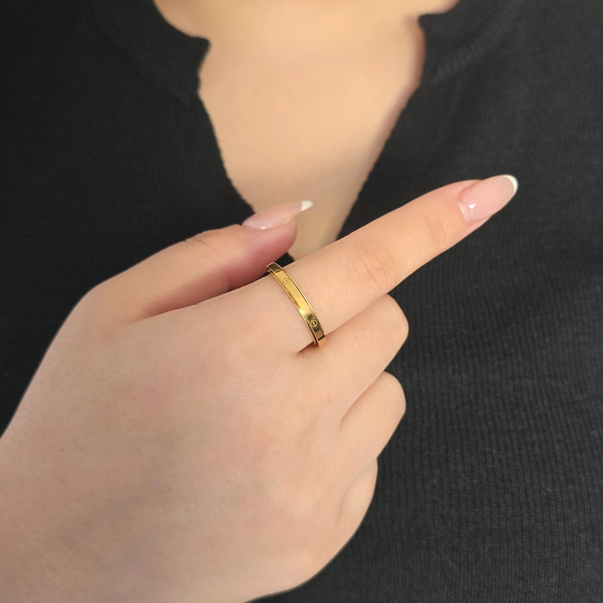 Detailopname van een gouden fidget ring met elegante, in kleine cirkels gegraveerde golfjes aan de wijsvinger van een model met een zwart topje.