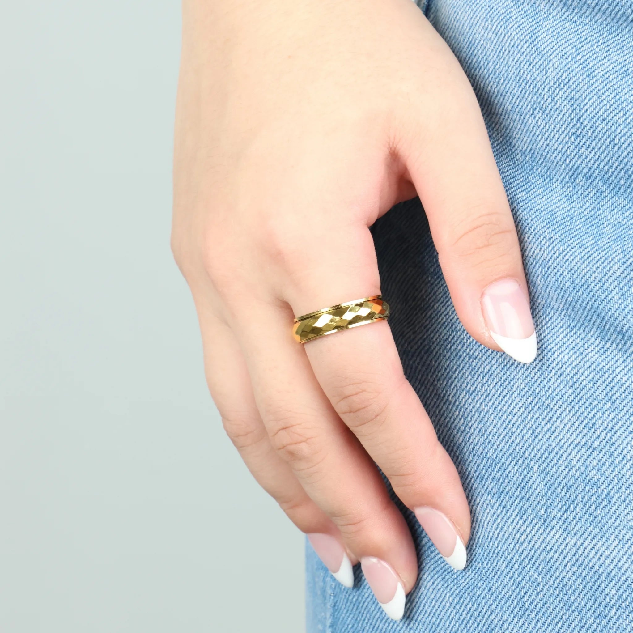 Gouden Nova fidget ring met gehamerde band, gedragen bij denim in natuurlijk licht