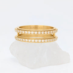 Gouden Gemini fidget ring met een opvallende dubbele band vol fonkelende kristallen, gepresenteerd op een witte steen.