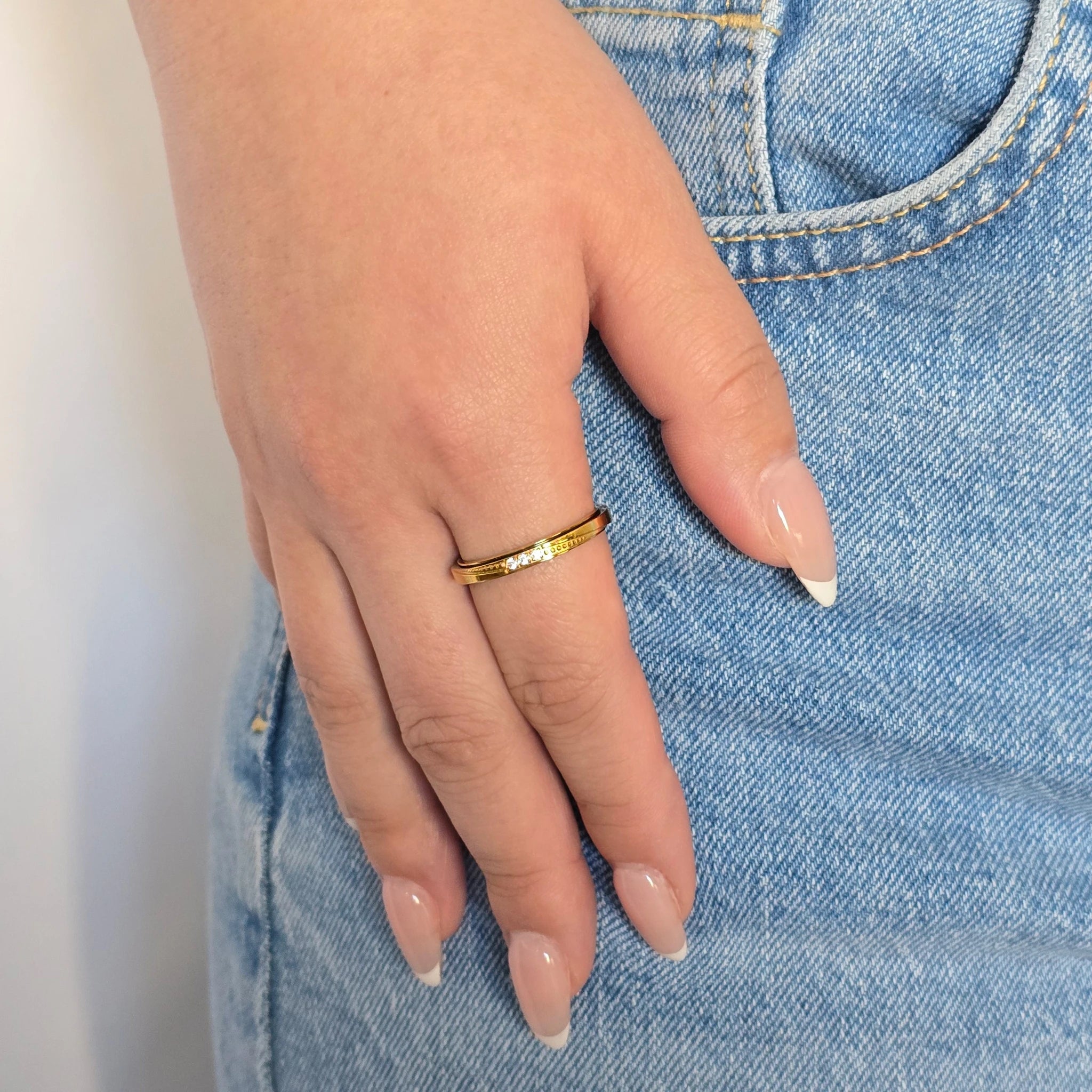 Hand van een vrouw in een blauwe jeans met een verfijnde gouden anti-stress ring met kristallen aan haar vinger.