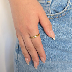 Hand van een vrouw in een blauwe jeans met een verfijnde gouden anti-stress ring met kristallen aan haar vinger.
