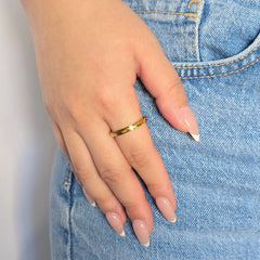 Hand van een vrouw in een casual blauwe jeans met een gouden anti-stress ring met infinity symbolen aan haar vinger.