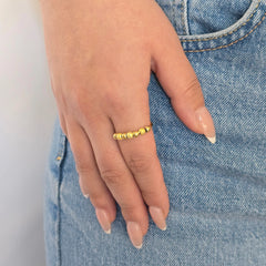 Hand van een vrouw in een casual blauwe jeans met een stijlvolle gouden anti-stress ring met balletjes aan haar vinger.
