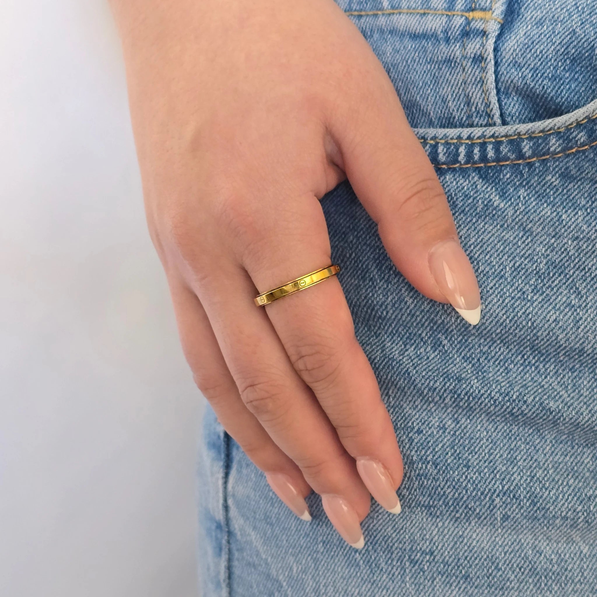 Hand van een vrouw in een casual blauwe jeans met een stijlvolle gouden anti-stress ring met een minimalistisch golfjespatroon aan haar vinger.