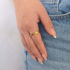 Hand van een vrouw in een casual blauwe jeans met een stijlvolle gouden anti-stress ring met een minimalistisch golfjespatroon aan haar vinger.