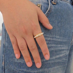 Hand van een vrouw met de gouden Perla anti-stress ring met parels om de vinger, gefotografeerd op een blauwe jeans.