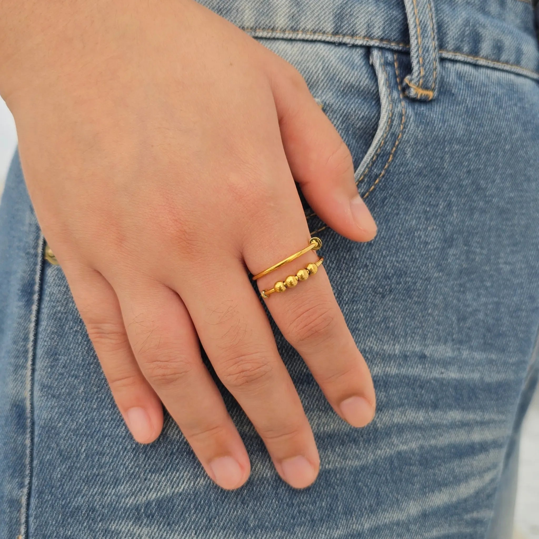 Hand van een vrouw met de gouden Punta Bead anti-stress ring met spijkerlook en draaibare kralen, gefotografeerd op een blauwe jeans.