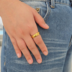 Hand van een vrouw met de gouden Trinity anxiety ring bestaande uit drie in elkaar grijpende RVS ringen, rustend op een blauwe spijkerbroek.