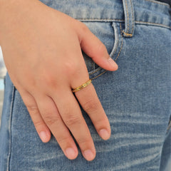 Hand van een vrouw met de gouden XO anxiety ring met roterend XO-motief, rustend op een blauwe spijkerbroek.