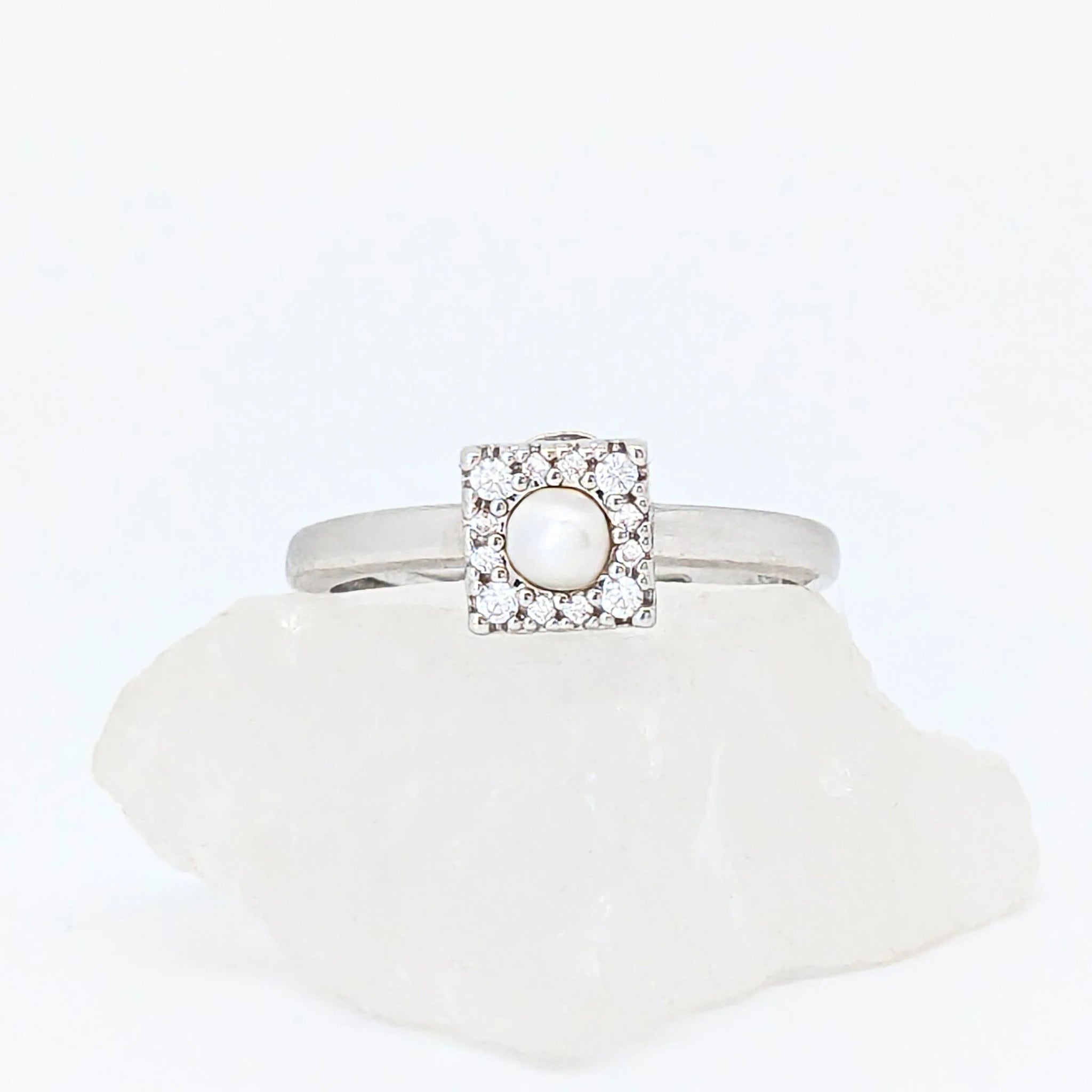 Zilveren Halo fidget ring met een glanzende parel in een vierkant frame, gepresenteerd op een witte ruwe steen.