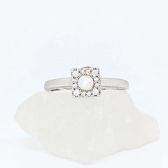 Zilveren Halo fidget ring met een glanzende parel in een vierkant frame, gepresenteerd op een witte ruwe steen.