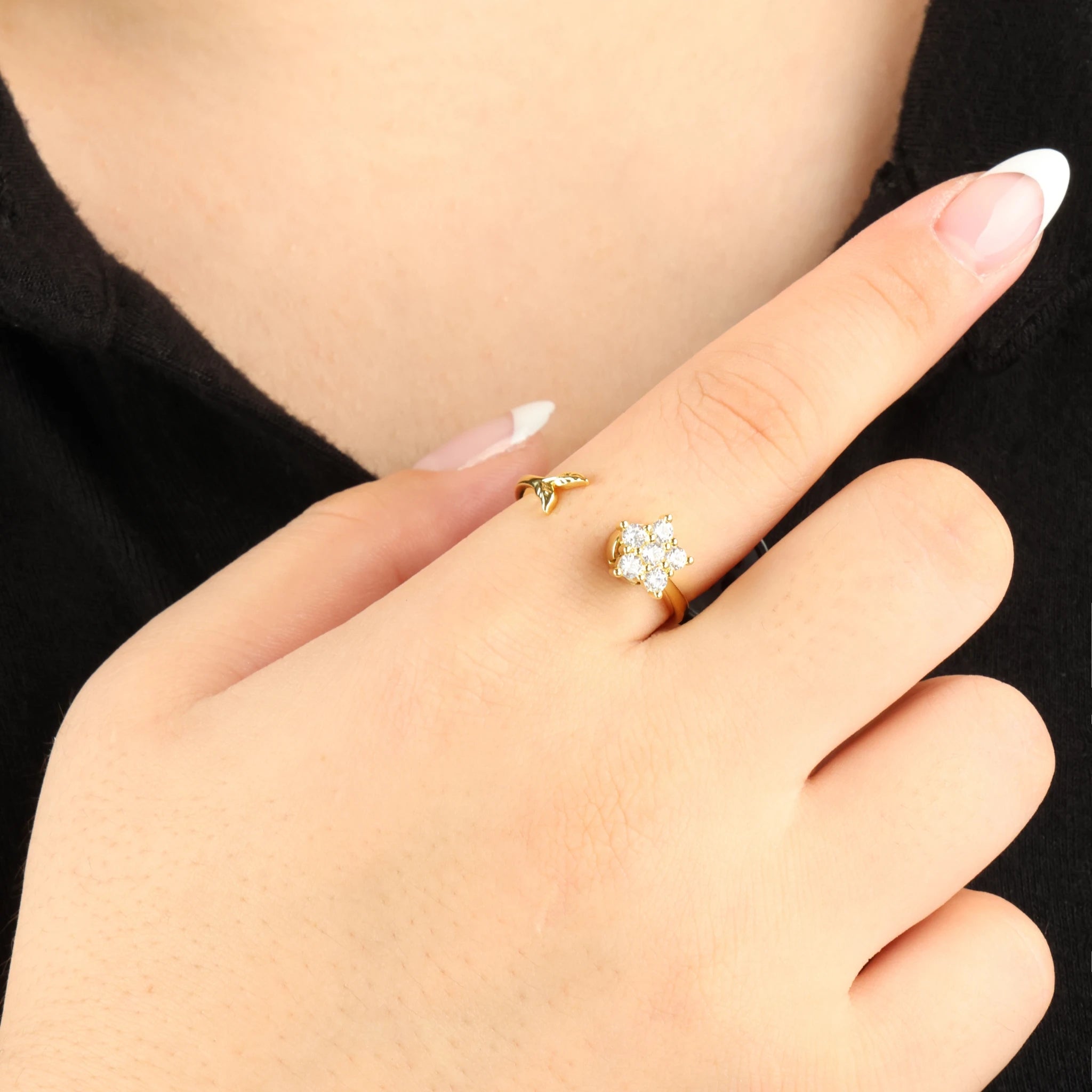 Gouden Iris anti-anxiety ring met een draaiend kristallen bloemetje om de vinger bij een zwart shirt.