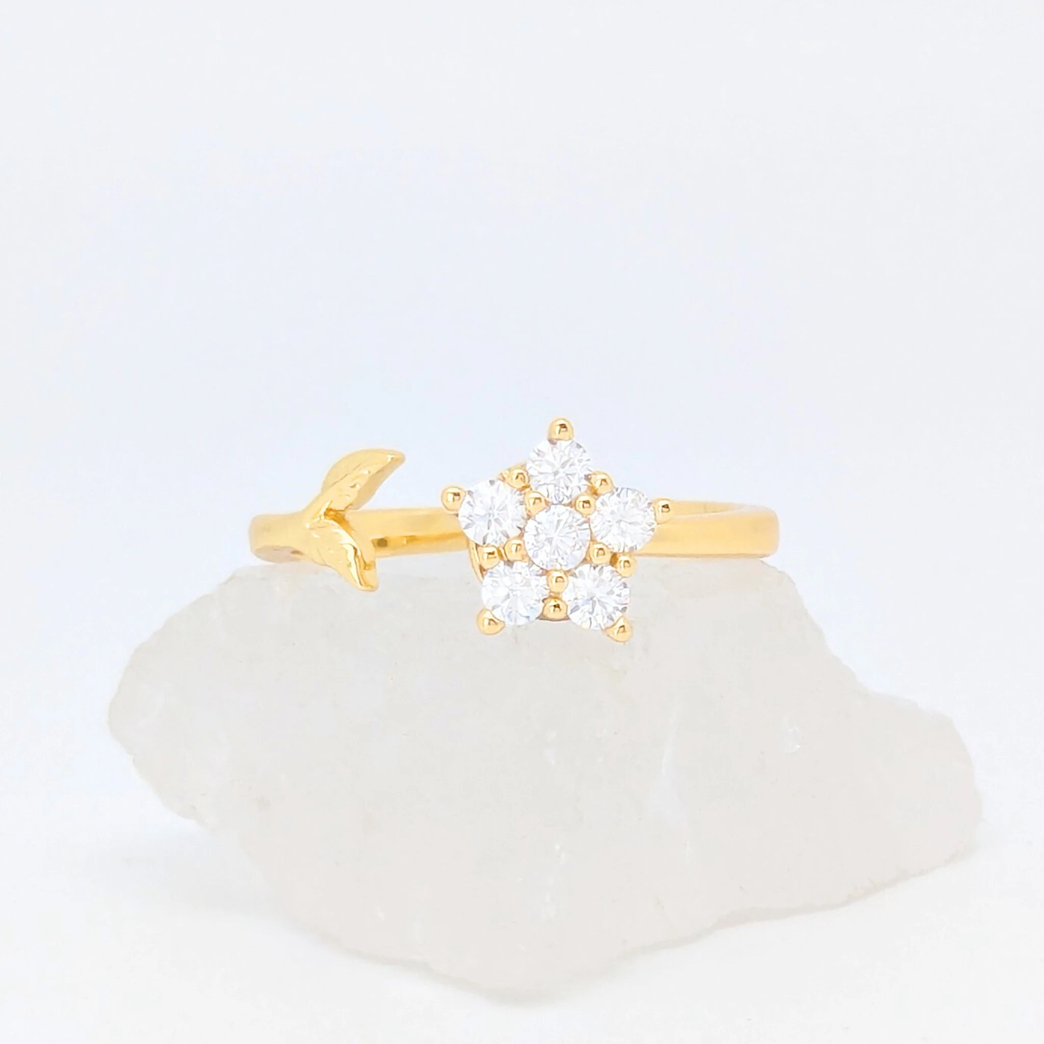 Gouden Iris fidget ring in de vorm van een bloem en een subtiel takje gepresenteerd op een witte ruwe steen.