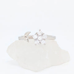 Zilveren Iris fidget ring met een glanzende bloem van kristallen en een verfijnd zilveren blaadje, liggend op een witte steen.
