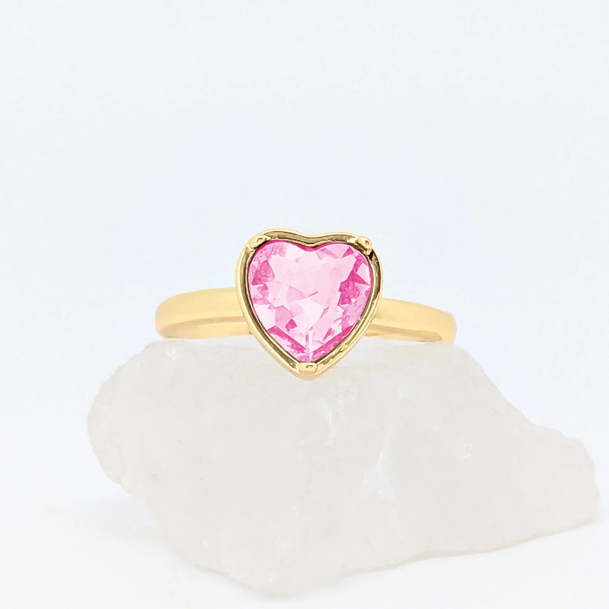 Gouden Love fidget ring met een glanzend roze hartje gepresenteerd op een witte ruwe steen.