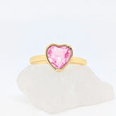Gouden Love fidget ring met een glanzend roze hartje gepresenteerd op een witte ruwe steen.