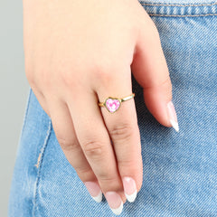 Draaiende gouden Love stress ring met een roze kristallen hart om een vinger tegen een jeans achtergrond.