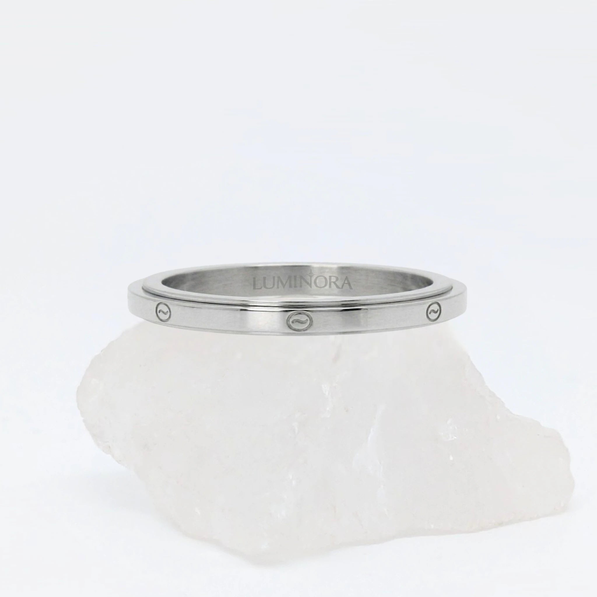 Zilveren Marea anxiety ring gekenmerkt door een strak design met subtiele golfmotieven, geplaatst op een witte kwartssteen.