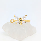 Gouden Nabi fidget ring met een elegante sprankelende vlinder liggend op een witte ruwe steen.