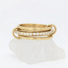 Gouden Neo fidget ring van RVS met een opvallend design van drie gestapelde ringen en glimmende steentjes, elegant rustend op een witte steen.