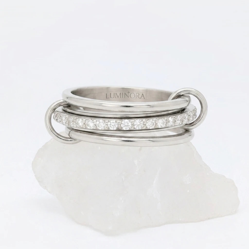 Zilveren Neo fidget ring van RVS opgebouwd uit drie ringen met een roterende middelste band vol zirkonia steentjes, gepresenteerd op een witte steen.