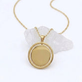 Gouden Oracle fidget ketting van RVS met een draaibare hanger, geplaatst op een witte steen.