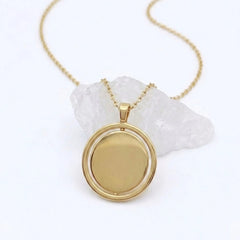 Gouden Oracle fidget ketting van RVS met een draaibare hanger, geplaatst op een witte steen.