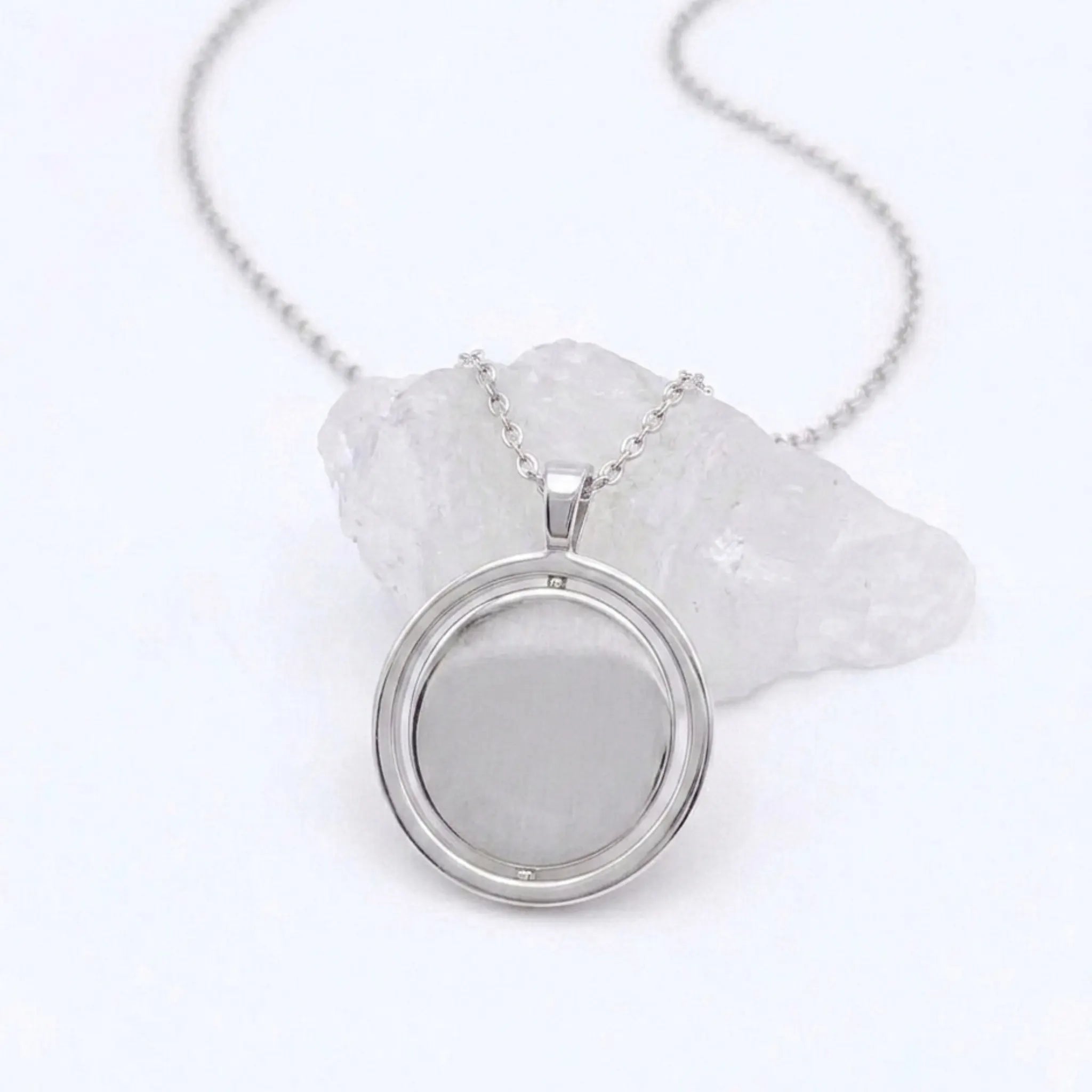 Zilveren Oracle fidget ketting van RVS met een roterend hangerontwerp, elegant gepresenteerd op een witte steen.