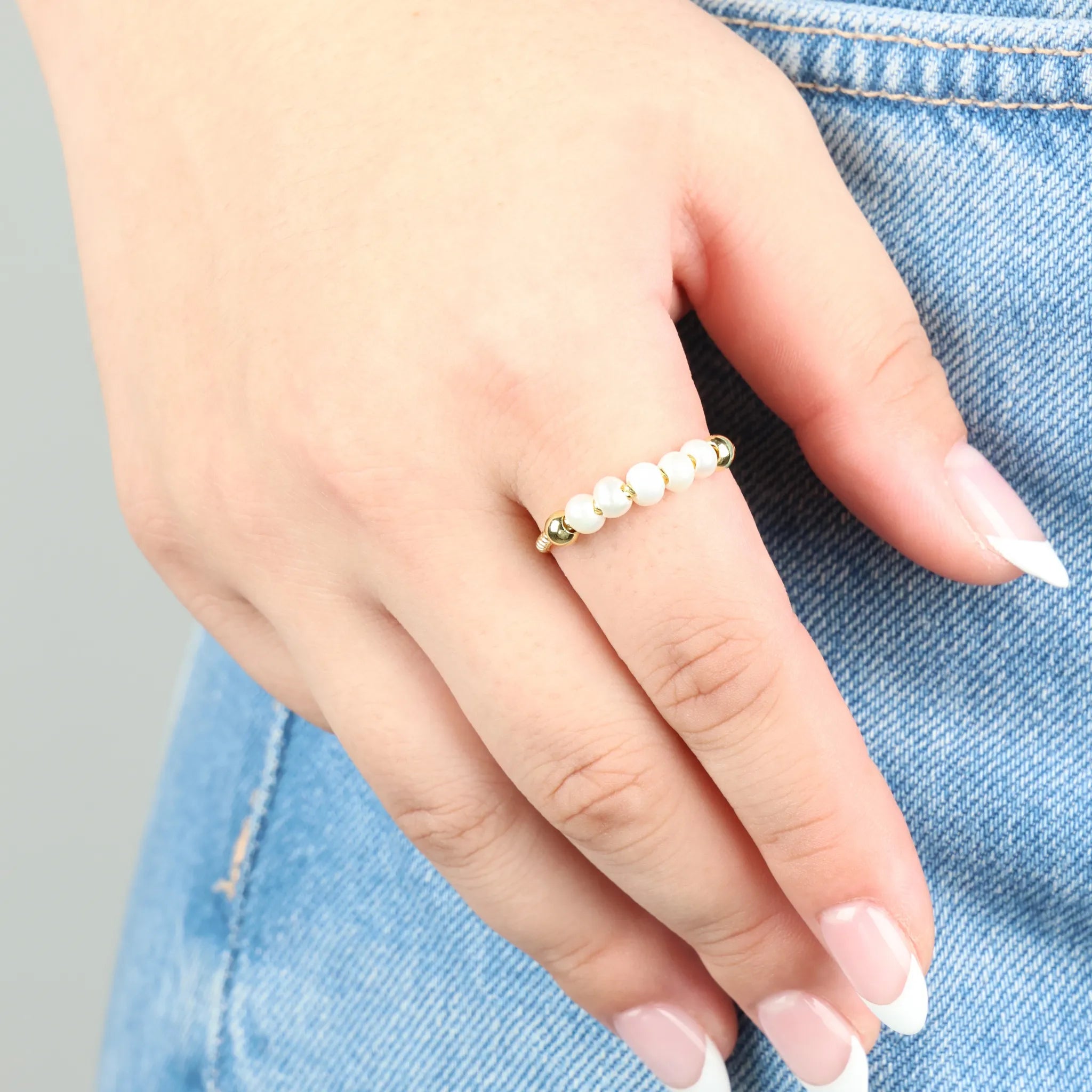 Vrouw draagt gouden Pearl fidget ring met parels bij spijkerbroek – Luminora