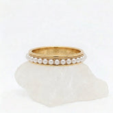 Gouden Perla fidget ring van RVS met een draaiende band van witte parels, gepresenteerd op een witte steen.