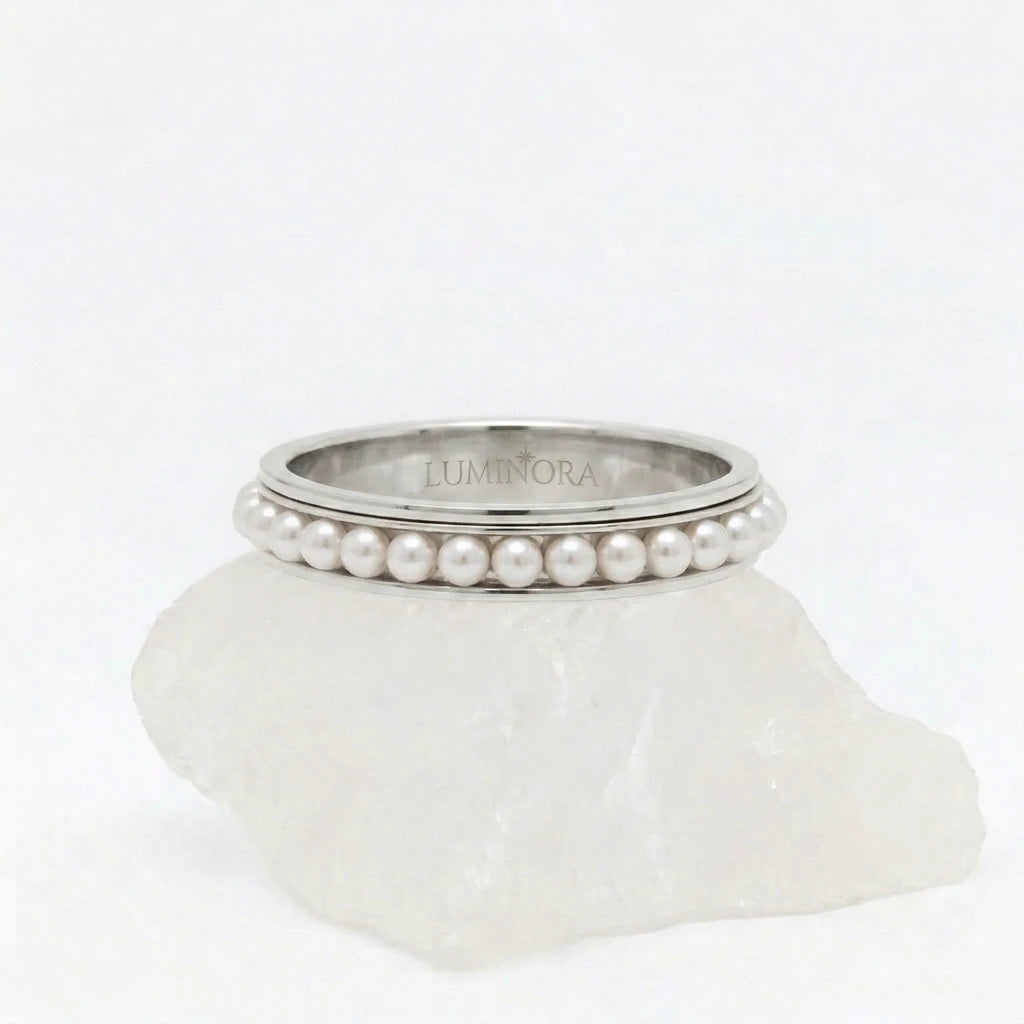 Zilveren Perla fidget ring van RVS met een roterende parelrand, elegant geplaatst op een witte steen.