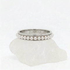 Zilveren Perla fidget ring van RVS met een roterende parelrand, elegant geplaatst op een witte steen.