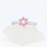 Zilverkleurige Petal fidget ring met een bloemvorm van heldere roze steentjes, gepresenteerd op een witte steen.