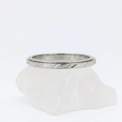 Zilveren Prism anxiety ring met een modern design van diagonale lijnen en facetten, elegant gepresenteerd op een witte steen.