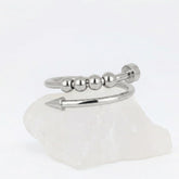 Zilveren Punta Bead fidget ring van RVS in het design van een gebogen spijker met beweegbare kralen, rustend op een witte steen.